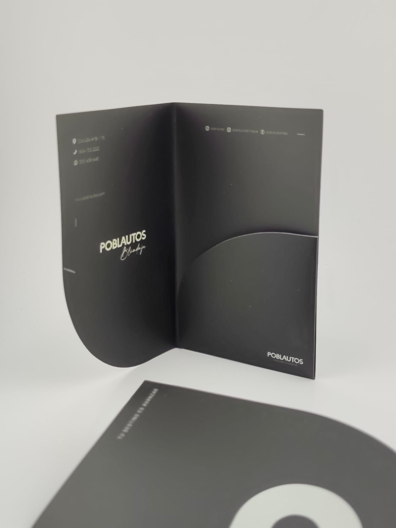 Carpeta corporativa abierta de pie mostrando el interior con bolsillo de corte curvo y datos impresos en plateado