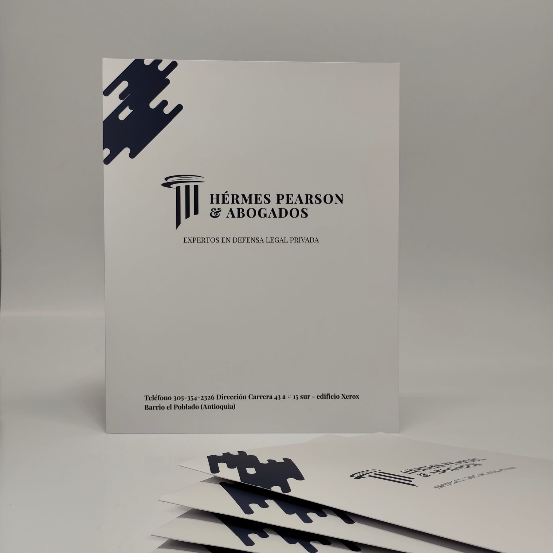 Carpeta de presentación blanca para un despacho de abogados, de pie sobre fondo neutro, con varias carpetas impresas abanicadas al frente